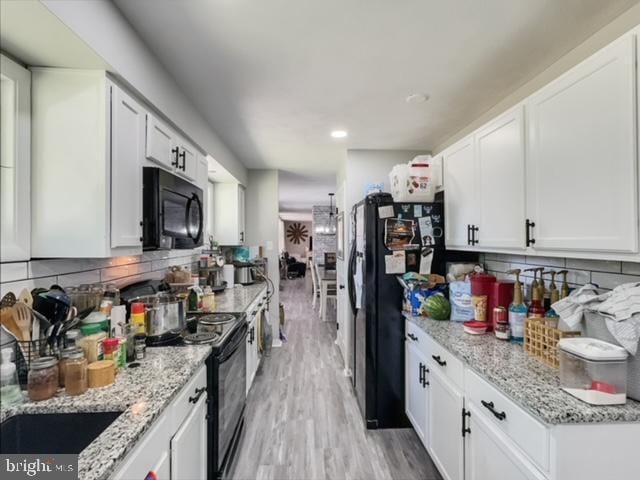 kitchen featuring black appliances, light stone countertops, light hardwood / wood-style floors, white cabinetry, and decorative backsplash