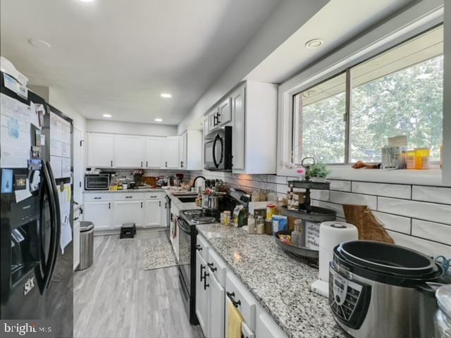 kitchen featuring black appliances, light stone countertops, tasteful backsplash, white cabinetry, and light wood-type flooring