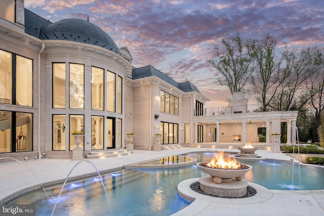 pool at dusk with pool water feature, a patio area, and an outdoor fire pit