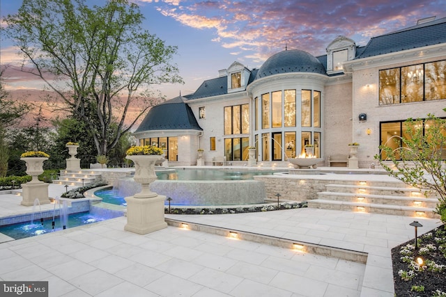 back house at dusk featuring pool water feature and a patio area