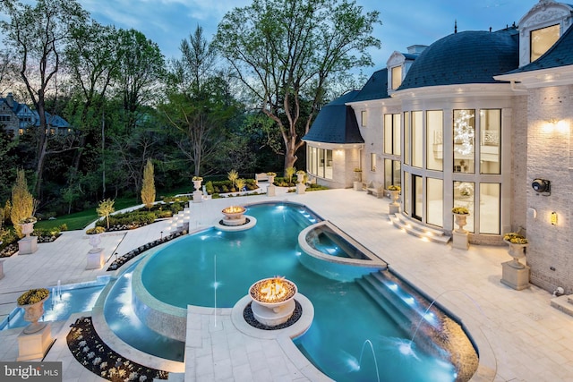 pool at dusk featuring a patio area, an in ground hot tub, and pool water feature