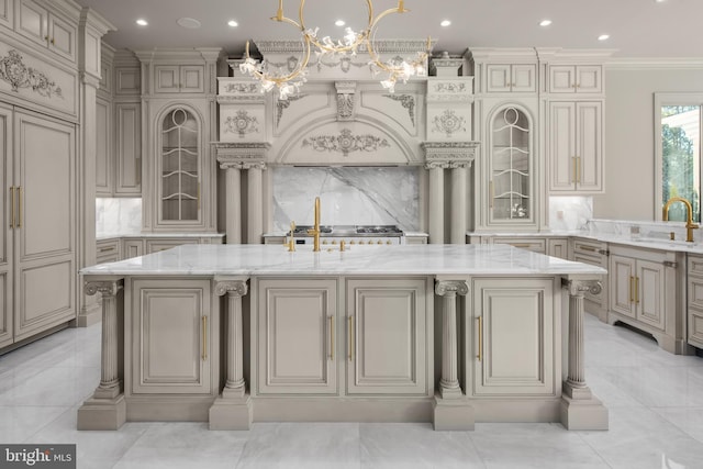 kitchen featuring decorative backsplash, a kitchen island with sink, cream cabinets, and light stone counters