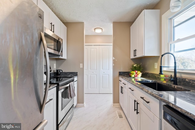 kitchen with sink, white cabinetry, stainless steel appliances, and dark stone counters