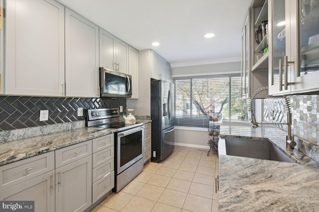 kitchen with backsplash, crown molding, light tile patterned floors, appliances with stainless steel finishes, and light stone counters