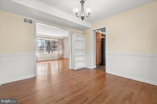 empty room with hardwood / wood-style flooring and an inviting chandelier