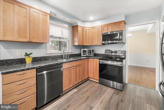 kitchen featuring appliances with stainless steel finishes, light hardwood / wood-style flooring, dark stone countertops, and sink