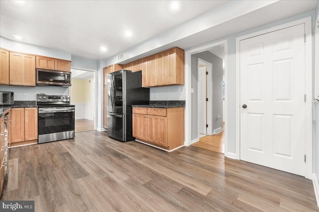 kitchen with hardwood / wood-style flooring, stainless steel appliances, and dark stone counters