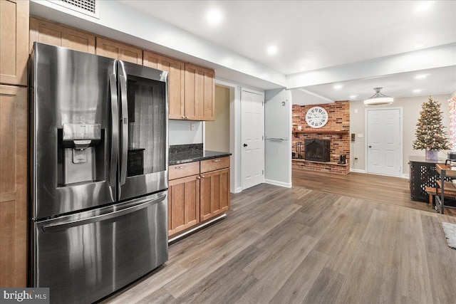 kitchen with a fireplace, stainless steel fridge with ice dispenser, dark stone counters, and wood-type flooring