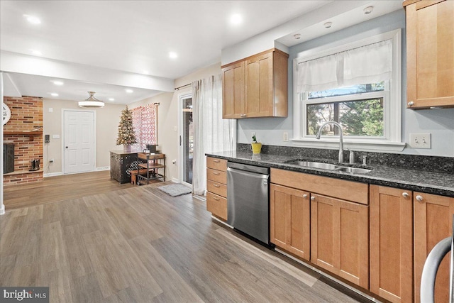 kitchen featuring a brick fireplace, stainless steel dishwasher, dark stone counters, sink, and light hardwood / wood-style floors