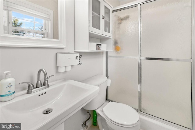 bathroom with toilet, a shower with door, and sink