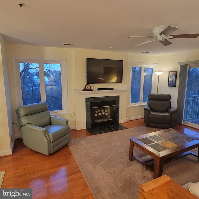 living room featuring a high end fireplace, wood-type flooring, and ceiling fan