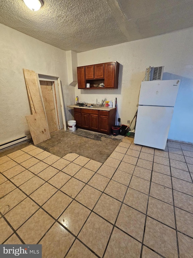 kitchen featuring white fridge, light tile patterned floors, a textured ceiling, and baseboard heating