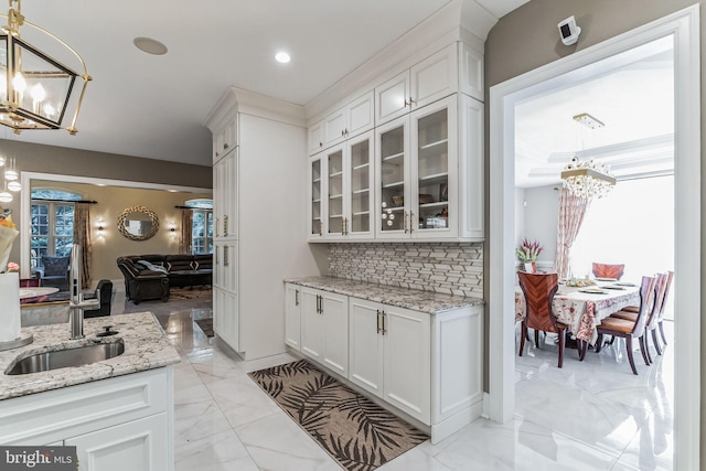 kitchen with white cabinetry, sink, light stone counters, pendant lighting, and decorative backsplash