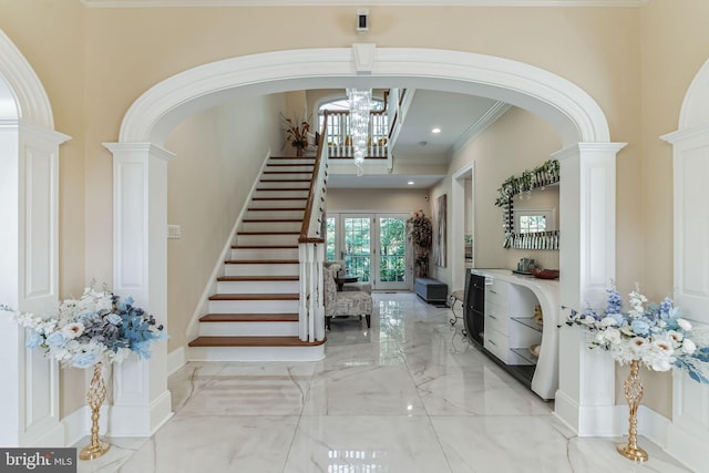 foyer entrance featuring an inviting chandelier, ornamental molding, french doors, and decorative columns