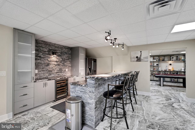 bar featuring gray cabinets, a paneled ceiling, dark stone counters, and wine cooler