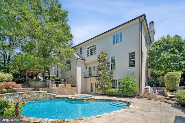 rear view of property with a pergola, a balcony, and a pool with hot tub