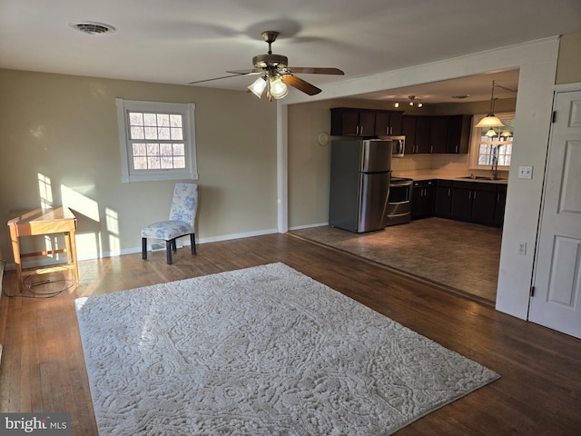 kitchen with appliances with stainless steel finishes, dark hardwood / wood-style flooring, dark brown cabinets, ceiling fan, and sink