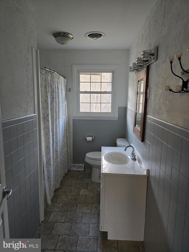 bathroom with walk in shower, vanity, tile walls, and toilet