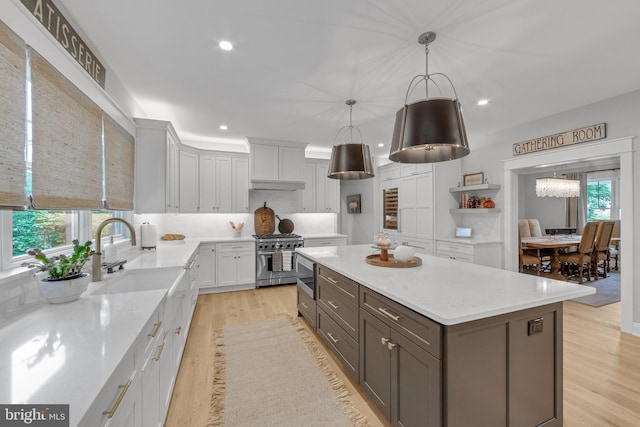 kitchen with white cabinets, light hardwood / wood-style flooring, appliances with stainless steel finishes, decorative light fixtures, and a kitchen island