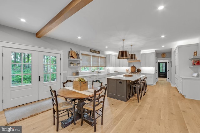 dining space with beam ceiling, sink, and light wood-type flooring