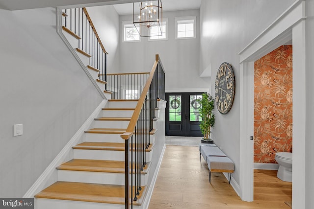 foyer with french doors, a towering ceiling, a notable chandelier, and light wood-type flooring