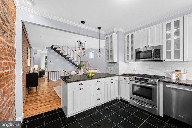 kitchen featuring brick wall, stainless steel appliances, dark tile patterned flooring, white cabinetry, and hanging light fixtures