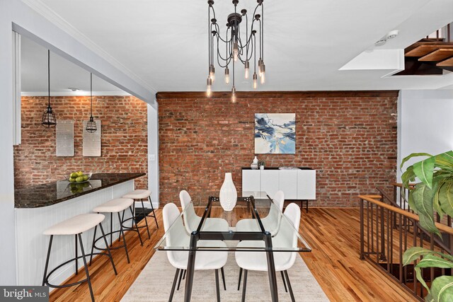 dining room featuring crown molding, brick wall, a notable chandelier, and light hardwood / wood-style floors