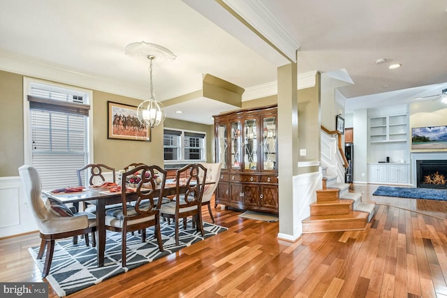 dining area with built in shelves, wood-type flooring, ornamental molding, and a chandelier