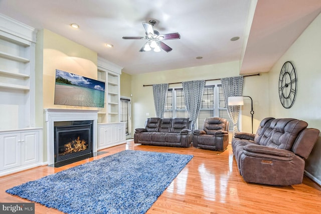 living room featuring ceiling fan, built in features, and wood-type flooring