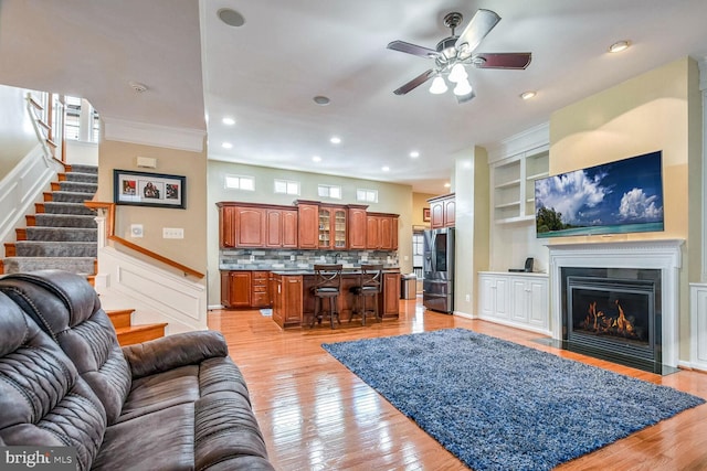 living room with ceiling fan, light wood-type flooring, ornamental molding, and built in shelves