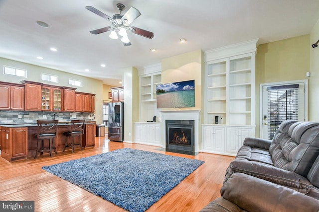 living room with built in shelves, ceiling fan, and light hardwood / wood-style floors