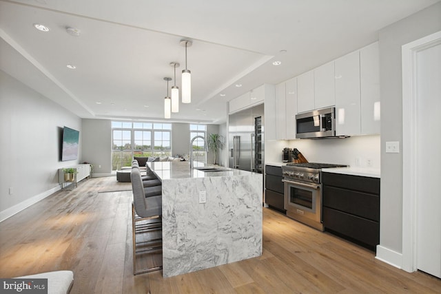 kitchen with appliances with stainless steel finishes, a breakfast bar, decorative light fixtures, white cabinetry, and an island with sink