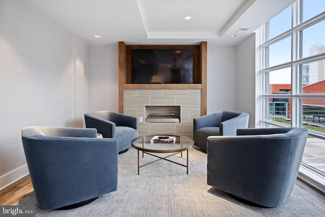 living room featuring a tray ceiling, a tile fireplace, and hardwood / wood-style floors