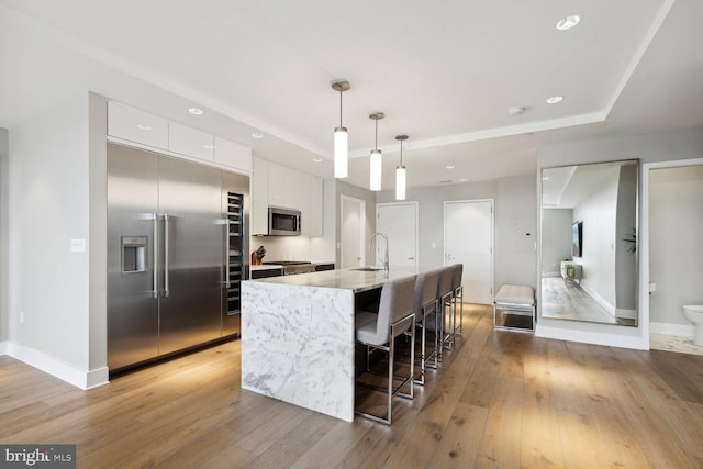 kitchen with white cabinetry, stainless steel appliances, light stone counters, an island with sink, and decorative light fixtures