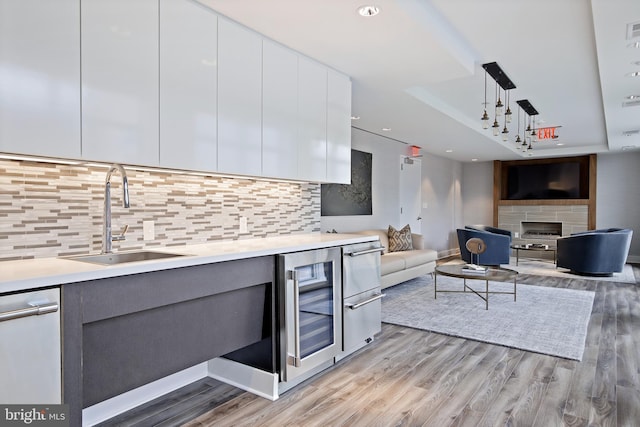 kitchen with backsplash, sink, light wood-type flooring, white cabinetry, and beverage cooler