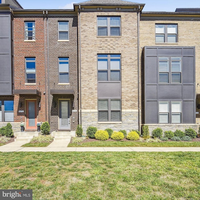 townhome / multi-family property featuring brick siding, stone siding, and a front lawn