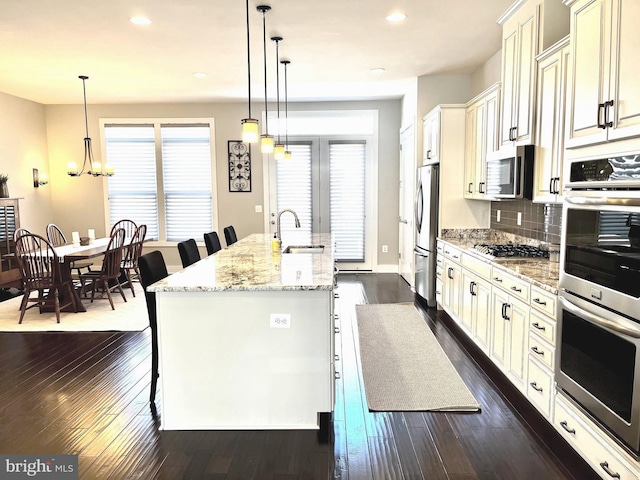 kitchen featuring a breakfast bar area, dark wood finished floors, an island with sink, a sink, and stainless steel appliances