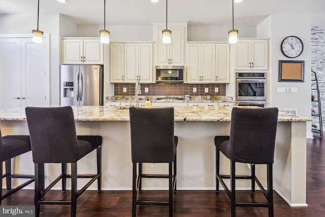 kitchen with a center island with sink, pendant lighting, light stone countertops, and appliances with stainless steel finishes