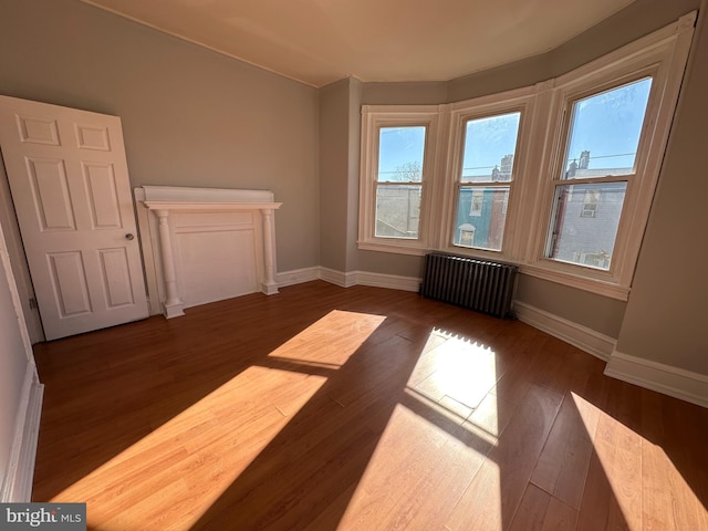 empty room with dark wood-style flooring, radiator heating unit, and baseboards