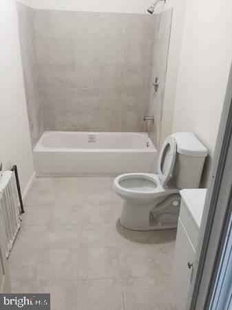 full bathroom featuring radiator heating unit, vanity, toilet, and tiled shower / bath combo