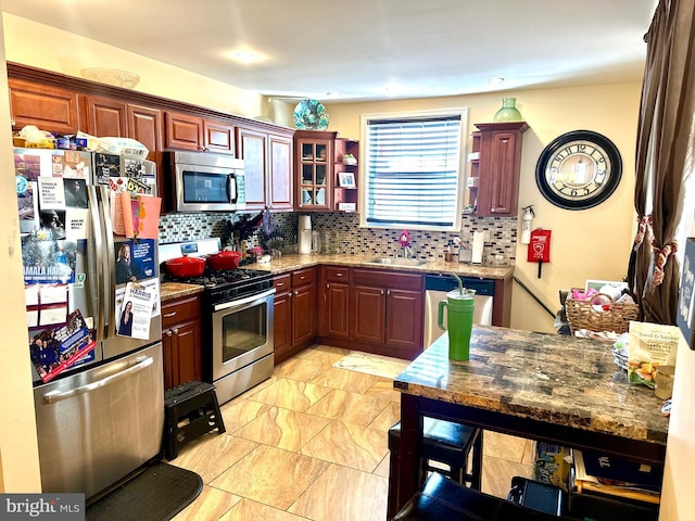 kitchen featuring decorative backsplash, stone counters, sink, and appliances with stainless steel finishes