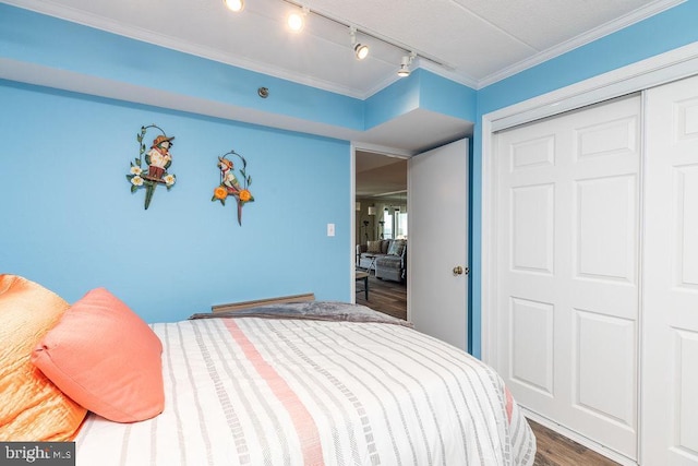 bedroom with track lighting, wood-type flooring, crown molding, and a closet