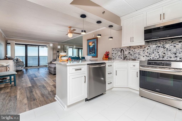 kitchen with kitchen peninsula, appliances with stainless steel finishes, white cabinets, and decorative light fixtures