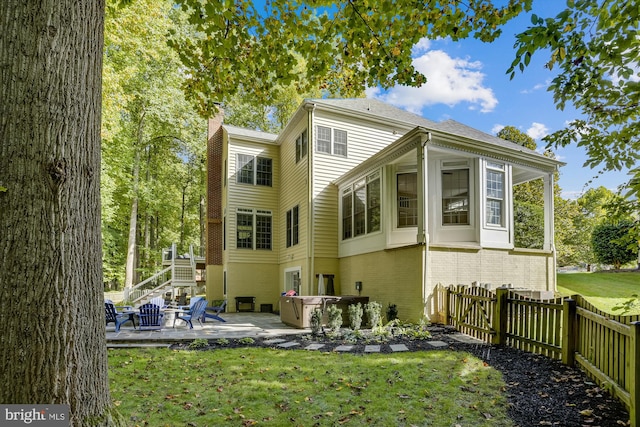 rear view of house featuring a jacuzzi, a patio, and a lawn