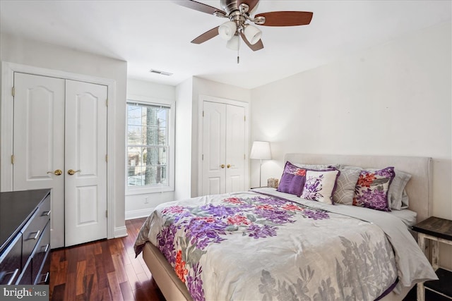 bedroom with two closets, ceiling fan, and dark hardwood / wood-style floors