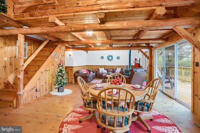 dining room featuring beamed ceiling, wood walls, light wood-type flooring, and wood ceiling