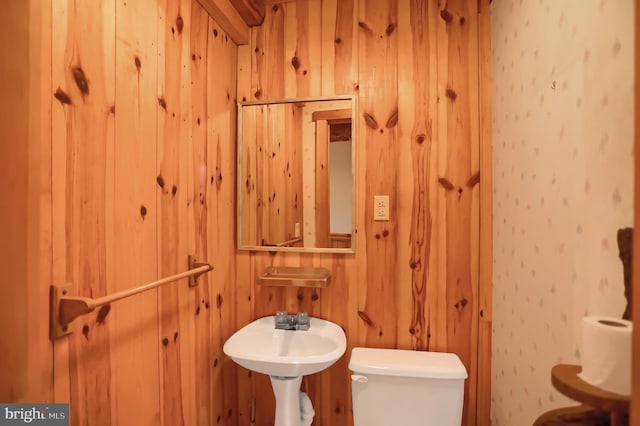 bathroom with toilet, wooden walls, and sink