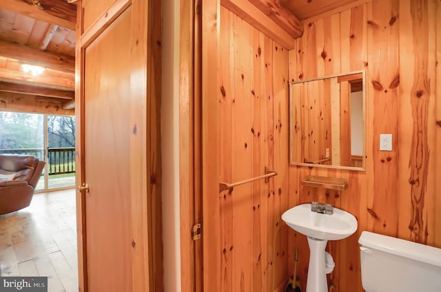 bathroom with beamed ceiling, toilet, hardwood / wood-style floors, and wooden walls