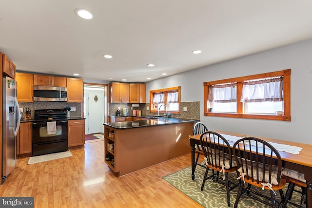 kitchen with kitchen peninsula, dark stone counters, stainless steel appliances, sink, and light hardwood / wood-style floors