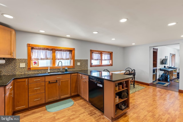 kitchen with sink, light hardwood / wood-style flooring, dark stone countertops, black dishwasher, and kitchen peninsula